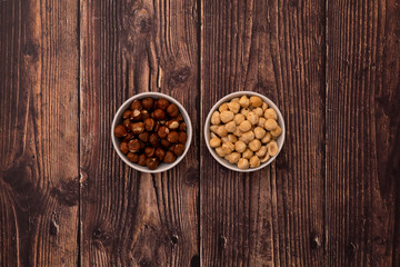Roasted and raw hazelnuts in bowls on wood background. Healthy snacks.