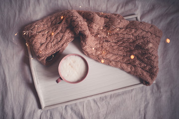 Tasty coffee with milk staying on tray with knited cloth in bed closeup. Top view. Winter season....