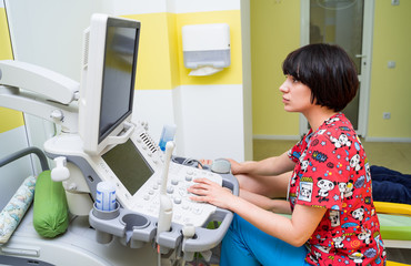 Doctor examining a boy with ultrasonic equipment at hospital. Closeup of a cheerfull female medician with special equipment.