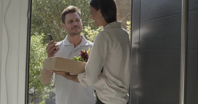 Female receiving package with vegetables at front door from delivery person