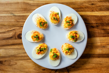 Overhead view of eight deviled eggs on a small white serving tray. Wood background, centered with copy space. 