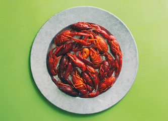 Several boiled crayfish or crawfish on a galvanized steel platter on a bright green background. Overhead view with copy space. 