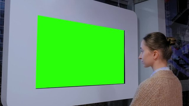 Green screen, mock up, future, copyspace, template, chroma key, technology concept. Woman looking at blank digital interactive green display wall at exhibition or museum with futuristic scifi interior