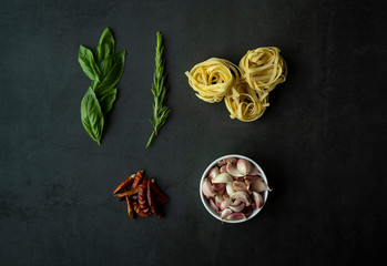 Garlic, fresh basil and rosemary, dry and hot pepper, tagliatelle on black background. Ingredients of italian pasta.