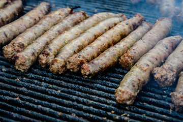 Mixed meat sausages being cooked on a hot black metallic grill in display for sale at a restaurant at a street food market, traditional food photographed with soft focus