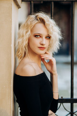 Fototapeta premium Incredible blonde woman with short haircut in black dress is leaning against wall