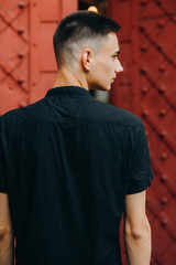 Fototapeta premium Sweet guy in the black shirt looks to the side on the gate background