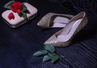 evening gold high-heeled shoes close-up on a dark table with a clutch bag and a black silk background
