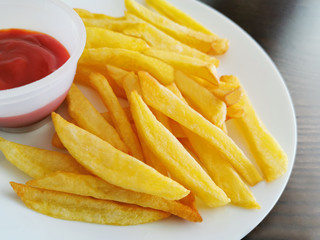 French fries or Potato fries and ketchup or tomato sauce on in a white plate on wood table. 