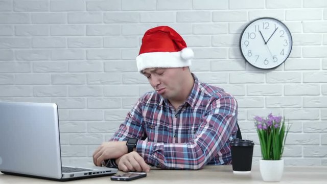 Portrait stressed displeased worried business man in santa hat sitting in front of laptop computer. Negative face expression emotion feelings problem perception