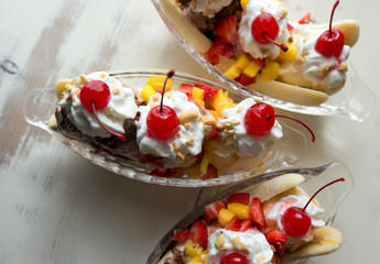 Close up of three banana splits with fresh fruit topping and whipped cream with maraschino cherries.  - obrazy, fototapety, plakaty
