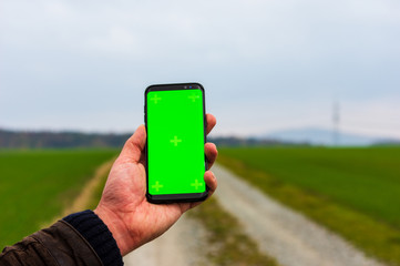 Hiking man with leather jacket using his smart phone to navigate in open autumn landscape. Using a cellphone to check map while doing outdoor activities in front of blurred landscape. Selective Focus
