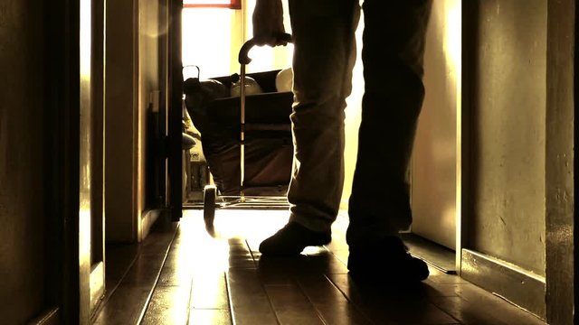 Backlit POV shot at ground level in strong sunlight, of a man pulling a laden shopping trolley up a step and along the floor into his home.