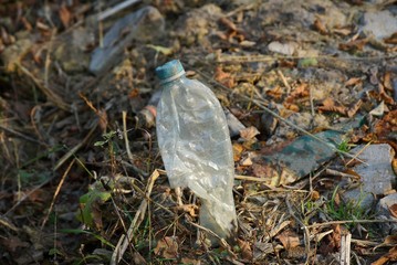 garbage from one gray plastic bottle on dry grass in the forest