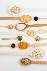 mixed pulses in wooden spoon. rice, red lentils, green lentils, corn, bulgur, dried mint, isot, black pepper, oregano, pasta, wire noodle, scallops.