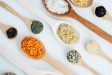 mixed pulses in wooden spoon. rice, red lentils, green lentils, corn, bulgur, dried mint, isot, black pepper, oregano, pasta, wire noodle, scallops.