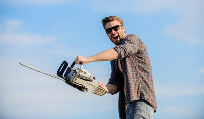 Naklejka premium Sharp blade. Dangerous job. Feeling manly. Powerful chainsaw. Handsome man with chainsaw blue sky background. Gardener lumberjack equipment. Lumberjack with chainsaw in his hands. Masculinity concept