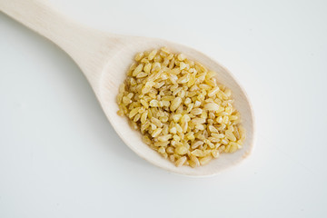 Bulgur grains in wooden spoon. On the white floor