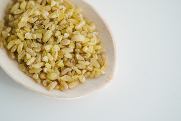 Bulgur grains in wooden spoon. On the white floor