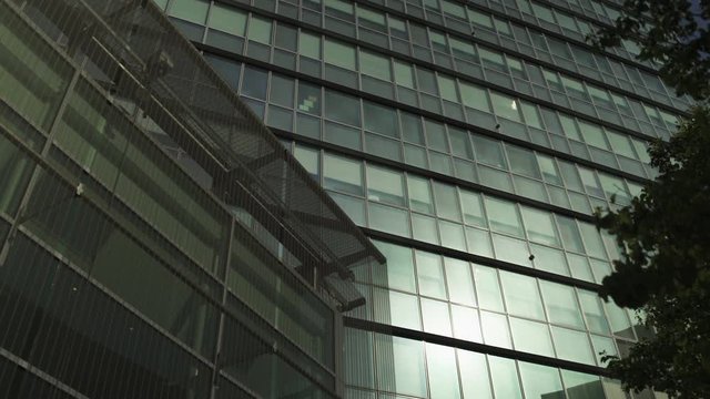 Grey Skyscraper with sun reflection, green glass windows at business district in Paris, slow steadicam movement tracking in, low angle shot. Futuristic modern building in Blue Sky. 4K.