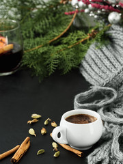 A cup of espresso and a glass of mulled wine on a black table and against the background of coniferous branches. Nearby spices are cinnamon and cardamom. Winter warming coffee. Close-up.