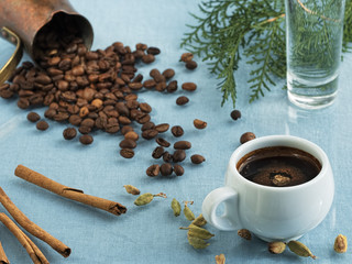 White cup of espresso and a glass of water on a blue canvas background. Next to the spices are...
