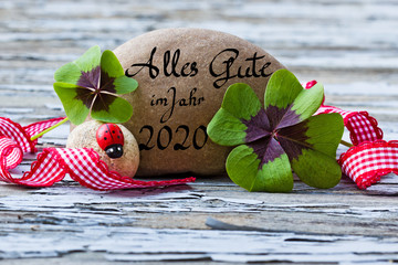 vierblättrige Kleeblätter, Marienkäfer und Stein auf Holz, Alles Gute im Jahr 2020