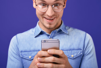Smiling young man types text in the mobile phone joyfully