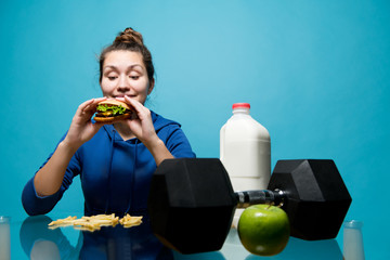 the girl looks with anticipation at the burger, and next to her lies a dumbbell, a bottle of milk...