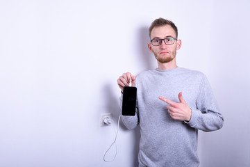  Serious gorgeous young man teenager connect his mobile phone to a charger on a socket on white...