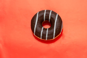 chocolate donut with white stripes on red background, top view