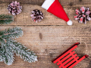 Snow-covered branches of a Christmas tree, cones, red sledges and Santa's hat.
