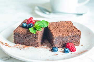 chocolate brownies cake decorated with mint and berries on a white plate