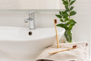 Fototapeta na wymiar Two bio-degradable, compostable bamboo toothbrushes on a towel in a bathroom white interior. Green plant decor in background.