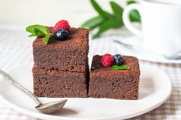 chocolate brownies cake decorated with mint and berries on a white plate
