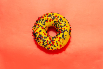 yellow donut with red and black powder on red background, top view
