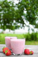 A glass of fresh cold smoothie with berries and cherrys on a wooden table, summer set, outdoor greed blured background,boke.