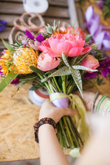 Girl bandages a bouquet of colorful flowers with a silk ribbon. Florist training workshop on creating flower bouquets. Floristics Studio.