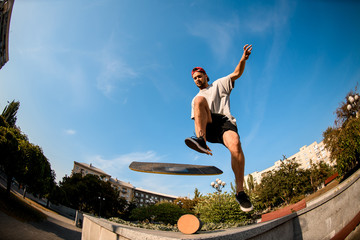 Fototapeta na wymiar Fish-eye shot man jumping on the balance board on the concrete border in the park