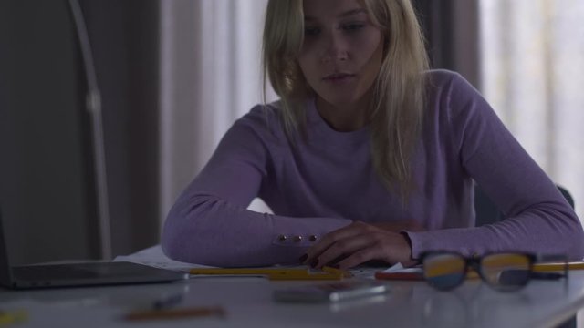 Sleeping Caucasian woman hearing mobile phone ring and waking up. Young tired professional architect or designer spending evening at work. Overwork, overload, hardworking.