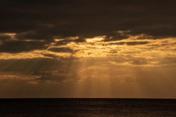 Dark cloudscape opening up with beams of sunlight shining through to Gulf of Mexico during sunset