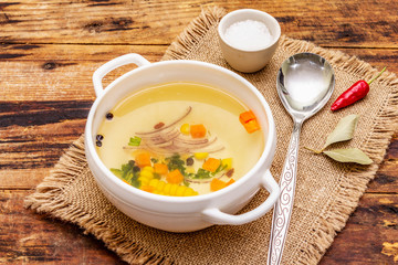 Transparent duck broth in bowl with vegetables. Traditional bouillon, healthy meal. Old wooden background