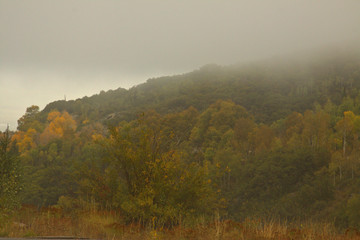 Fototapeta premium Mountain valley surrounded by fog with fall colors in the background
