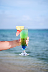 Woman holding cocktail on the beach overlooking ocean in Fiji