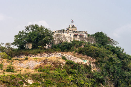 Nha Trang, Vietnam - March 11, 2019: Harbor control building and antenna on green forested hill above port under light blue sky.