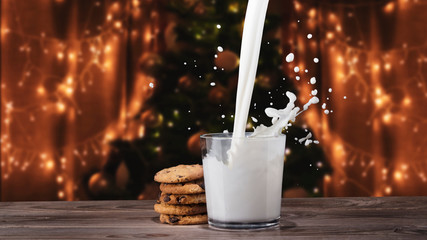 Glass of milk with cookies. Milk splashes. Backgroun of Christmas tree with decorations and bright...