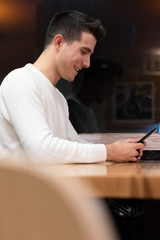 Fototapeta premium Young man sitting in coffee shop reading text message on mobile phone. Handsome caucasian guy at cafe using smart phone .