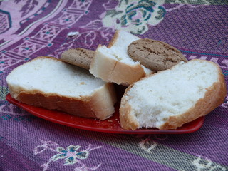 wheat white bread with oatmeal cookies on a glass red plate on a background of a motley tablecloth.
