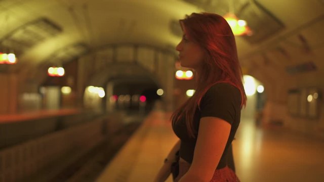 Cute redhead woman with freckles, piercings and red hair waiting at metro subway station, during sunny summer in Paris. Blurred underground background. 4K UHD.