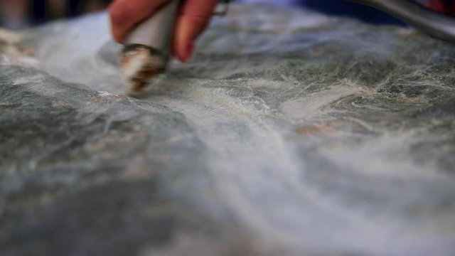 hand held close shot of hand carving a lime stone block with a wave-like pattern as a tourist attraction at Br&uacute; na B&oacute;inne in Newgrange. Daylight situation with natural light. 